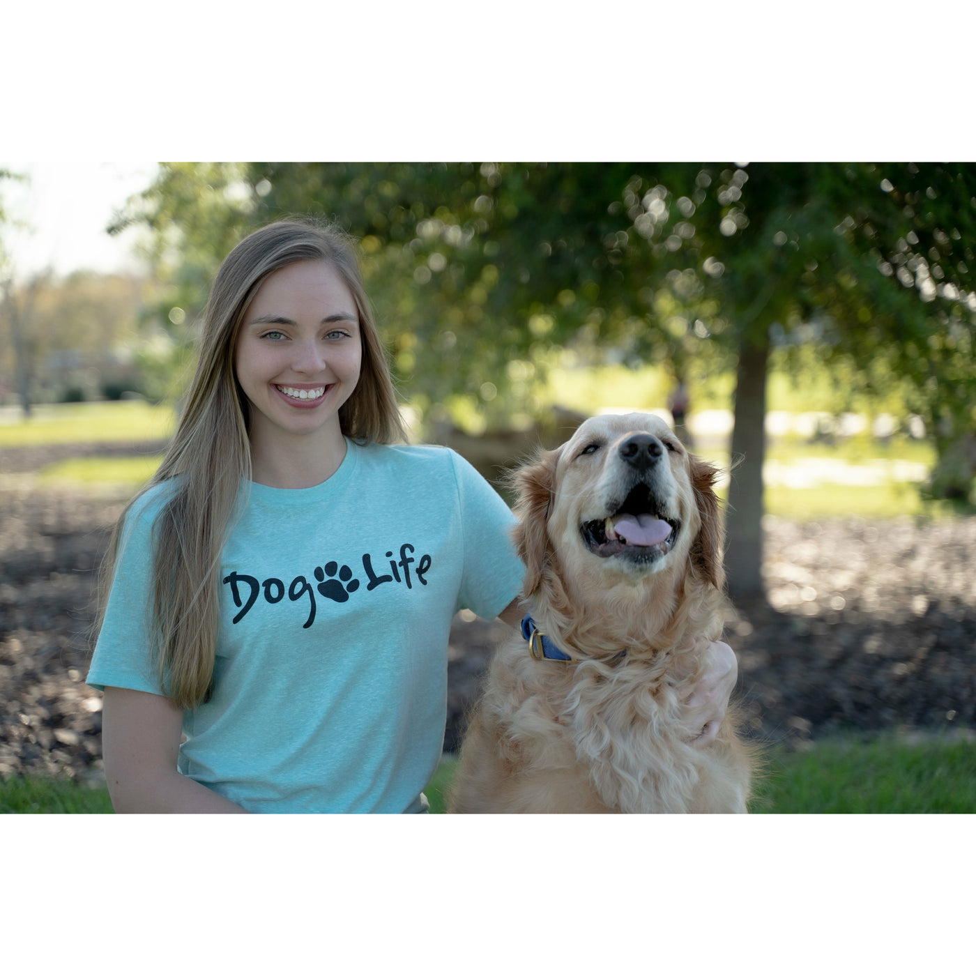 Young woman  wearing blue green Dog Life t-shirt with Golden Retriever  by her side