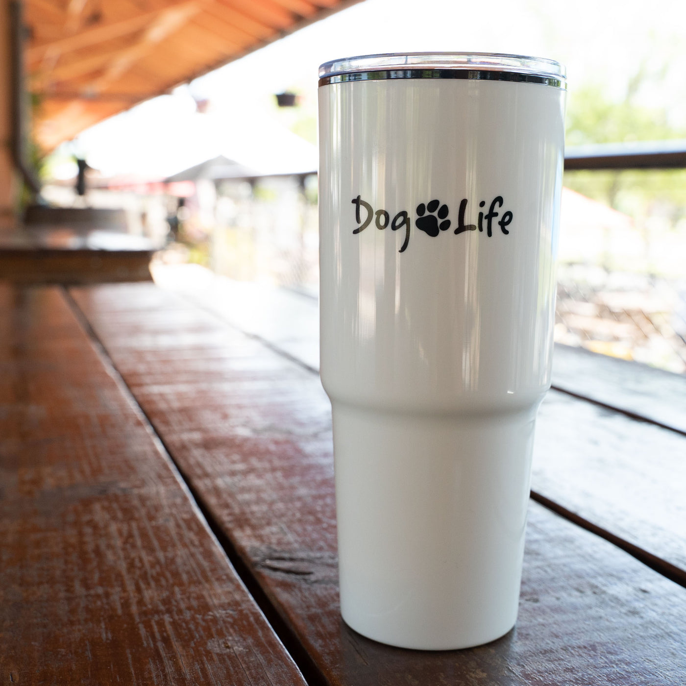 White tumbler with black Dog Life logo imprinted.  Tumbler is sitting on a wooden picnic table.