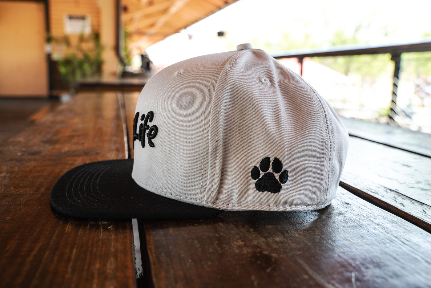 Side view of Dog Life snap back hat.   White cap with black visor and dog paw stitched on the left side of the hat